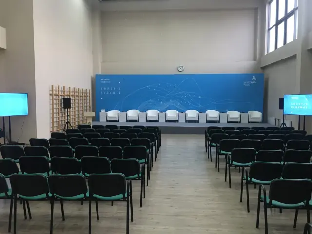 Конференц-зал с телевизорами на стойках по бокам сцены